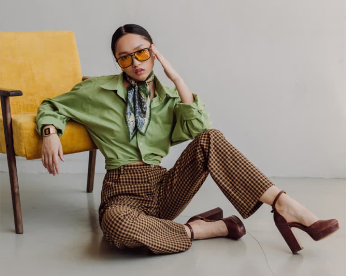 photo of a woman in gold shades, green scarf, a green shirt, brown pants and brown shoes